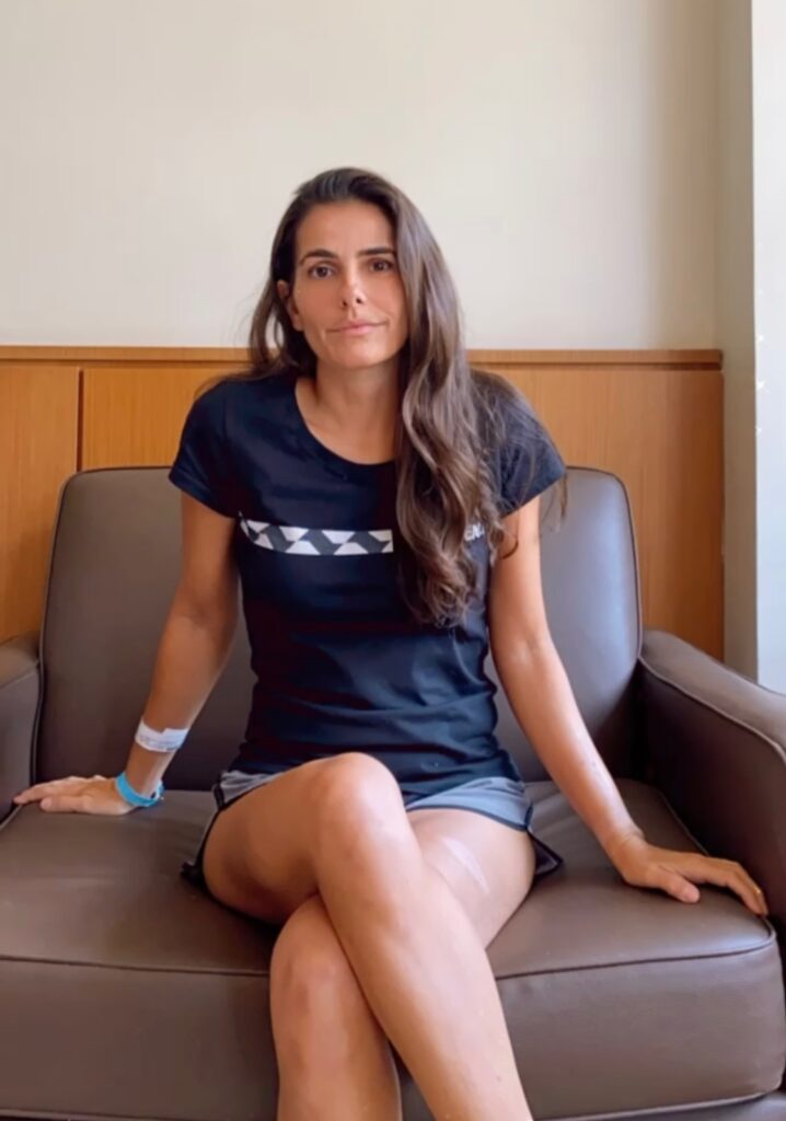 Na imagem a Dra. Luciana Haddad está sentada com as pernas cruzadas enquanto explica algo para câmera que está gravando.